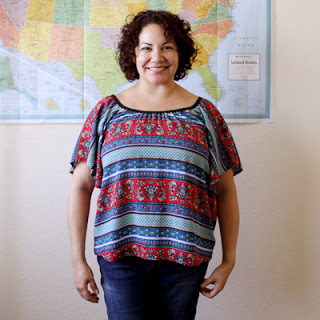 Curly haired woman standing in front of a map of the USA wearing a handmade Seamwork Loretta