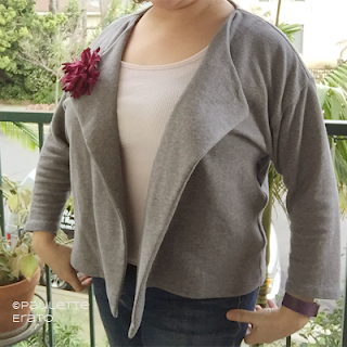 Cut off picture of a woman in a grey handmade Saunio cardigan over a pink top and with a purple flower pinned to her lapel