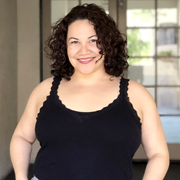 Curly haired Latina in a black tank with hands in pockets smiling at the camera