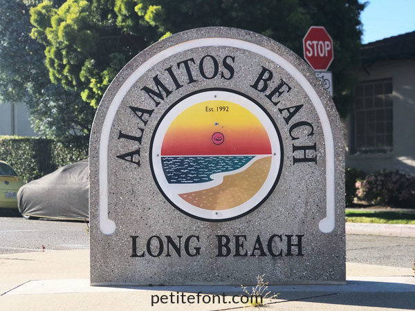 Large domed cement sign with image of sunset over the beach and text Alamitos Beach Long Beach