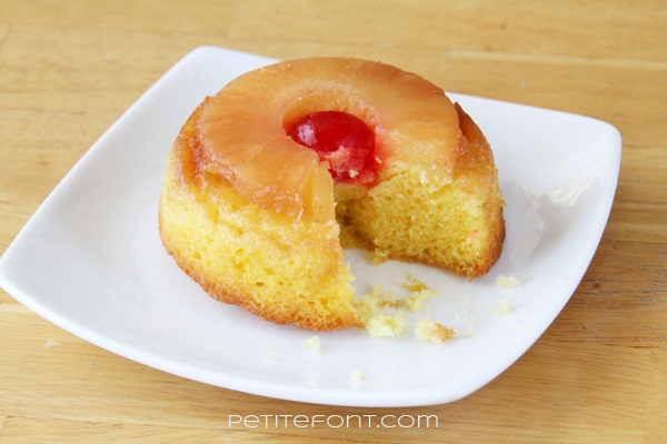 Single round serving of pineapple upside down cake with a bite missing, on a white plate, topped with a cherry