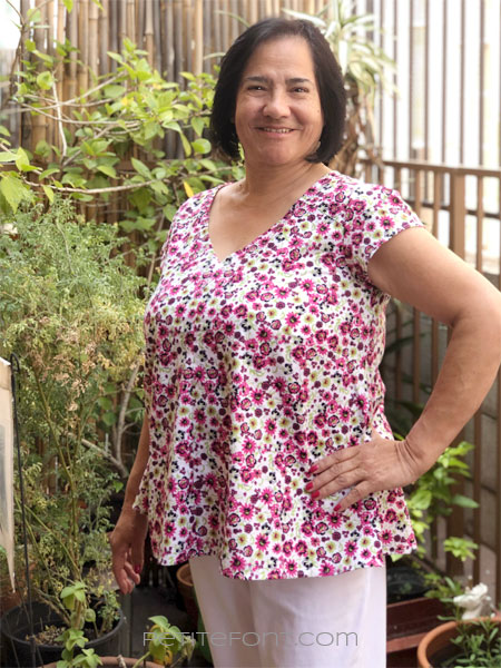 A woman with short black hair modeling New Look 6414 sewing pattern in floral quilting cotton, has her left hand on her hip and a big smile on her face