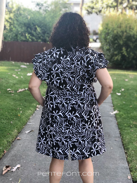 Back view of a curly haired brunette in shortened and narrowed Orchid dress in black and white floral fabric
