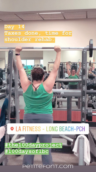 Image of a woman in a gym squat rack lifting a barbell over her head. Text overlay reads Day 14 Taxes done, time for shoulder rehab. LA Fitness-Long Beach-PCH hashtag the 100 day project hashtag 100 days of lbc Petite font dot com