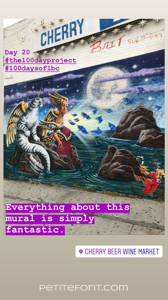 Image of an outdoor mural of a cat with angel wings and narwhal horn sitting on a rock next to a winged woman wings on her head, its tail in the water as blue birds fly away. A full moon in background behind lavender clouds. Text overlay reads Day 20 hashtag the 100 day project hashtag 100 days of lbc, Everythign about this mural is simply fantastic. Cherry Beer Wine Market. Petite font dot com.