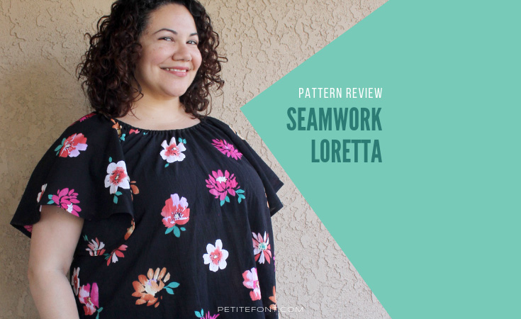 Curly haired brunette leaning against a stucco wall wearing a handmade Seamwork Loretta in black floral cotton gauze with green box and text overlay that reads Pattern Review Seamwork Loretta. Web address petite font dot com.