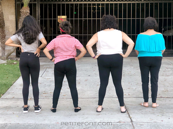 Back view of 4 women wearing black leggings as pants without their shirts covering their butts, with their arms on their waists
