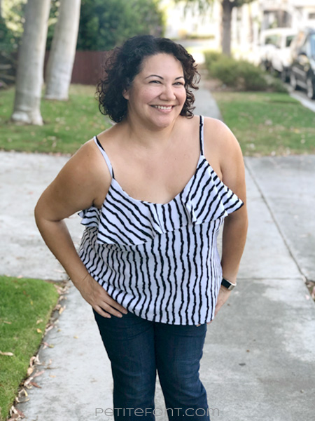 Curly haired Latina woman in a striped ruffled Ogden cami hack leaning forward with a smile on her face