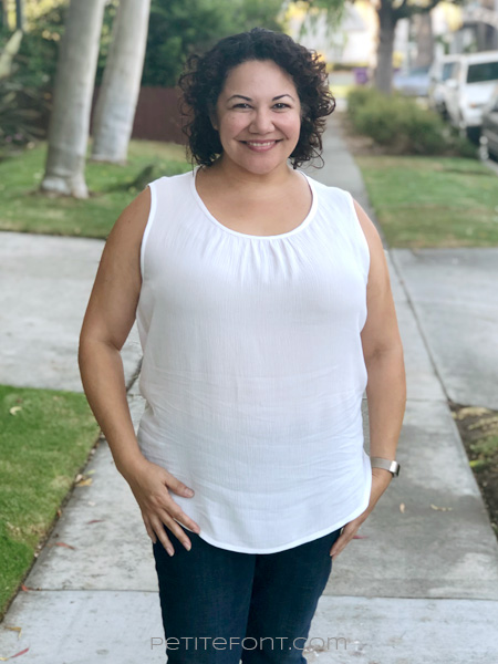 Latina curly haired woman in a white sleeveless hacked Daisy blouse untucked and skinny jeans facing forward