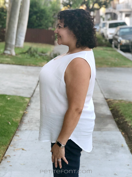 Latina curly haired woman in a white sleeveless hacked Daisy blouse and skinny jeans facing to the side