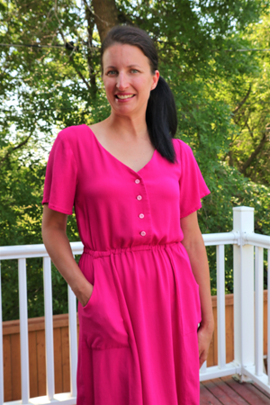 Dark haired woman in a pink dress with her hand in her pocket