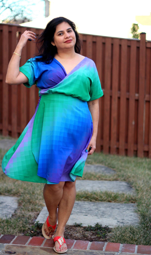 Dark haired woman in blue and green Rad Patterns Unicorn Dress wrap dress with one hand up near her hair.