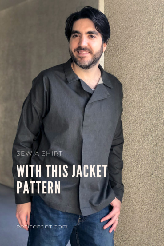 Dark haired man wearing a dark charcoal grey Ilford jacket as a shirt, with jeans, leaning up against a beige stucco wall with text overlay that reads Sew a Shirt with this Jacket Pattern, PetiteFont.com