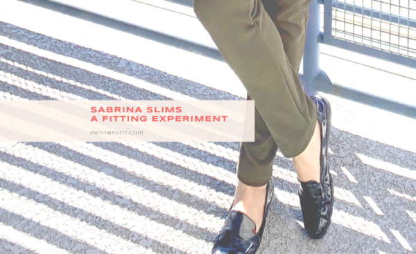 Image of person wearing olive green pants and patent leather loavers with the ankles crossed, a shadow across the ground of the railing behind them, and text overlay that reads Sabrina Slims, A Fitting Experiement, PetiteFont.com