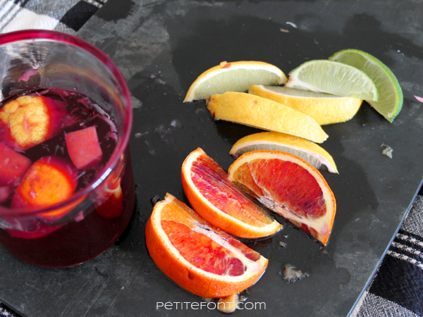 An overhead view of a glass of sangria on a black wooden cutting board with blood orange, lemon, and lime wedges cut open on top of it.