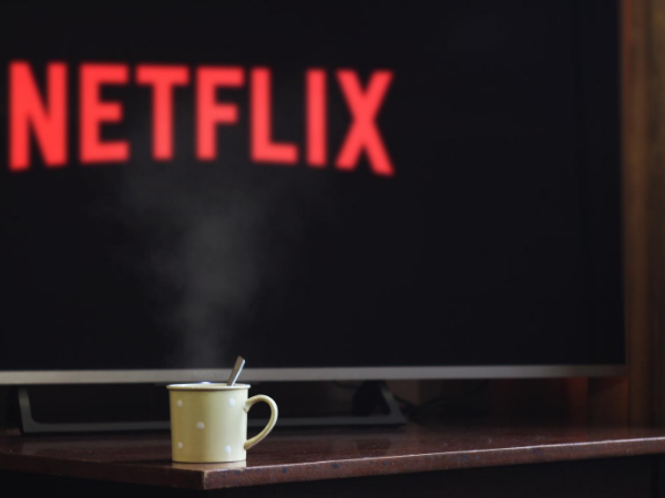 Coffee mug on table in front of a tv with the Netflix logo on it