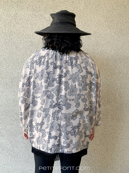 Paulette with her back to the camera wearing a black sun hat and a paisley version of Simplicity 1108 robe. The paisley pattern is on a light peach background.