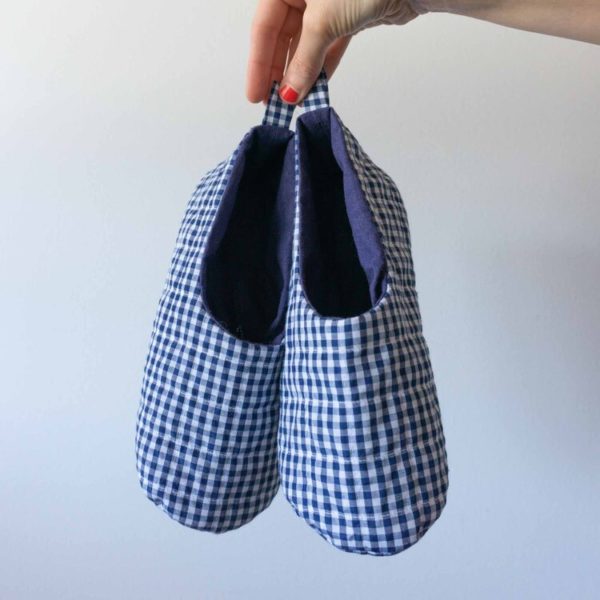 A hand holding a pair of blue gingham Sew DIY quilted booties against a white backdrop