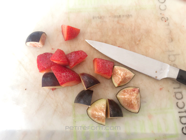 Chopped strawberries and figs on a cutting board with a small knife