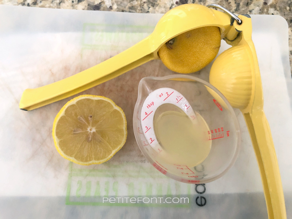 Half lemon sitting on a flexible cutting board with a hand juicer and an ounce of juice in a mini measuring cup