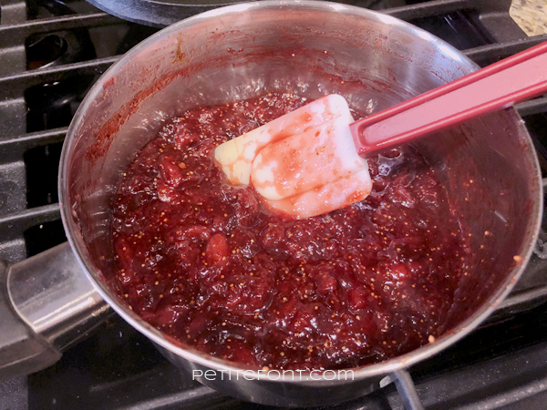 Saucepan on stove with a white spatula in the strawberry fig chipotle jam showing the right consistency to achieve