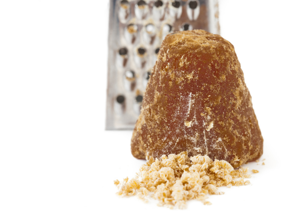 A cone of piloncillo with grated sugar in front, a box grater in the background