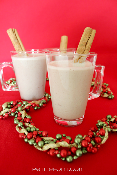 3 cups of coquito on a red background with Christmas garland around