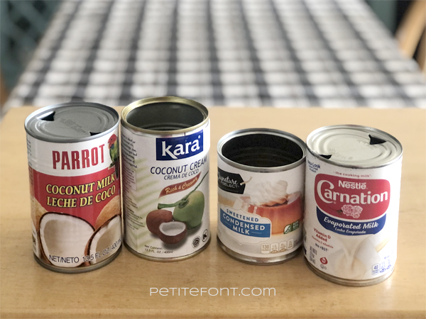 Four cans of coquito liquid ingredients against a wood background