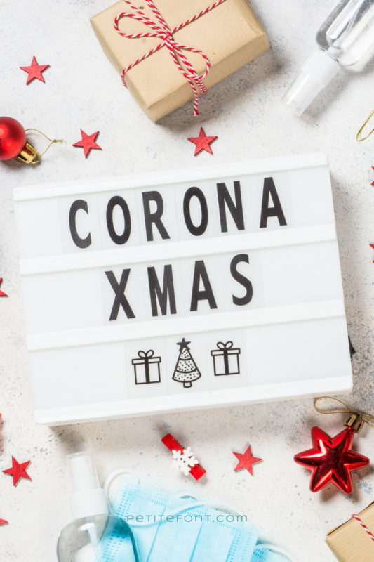 Gifts, holiday twine, masks, and gloves scattered around a lightbox with the words Corona Xmas spelled out