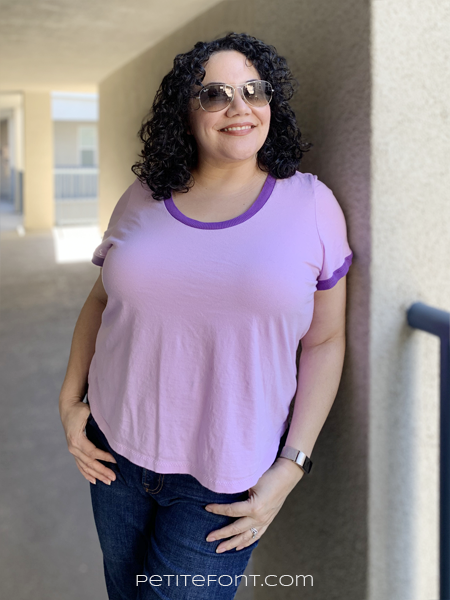 Paulette in a purple ringer tee leaning against a beige stucco wall