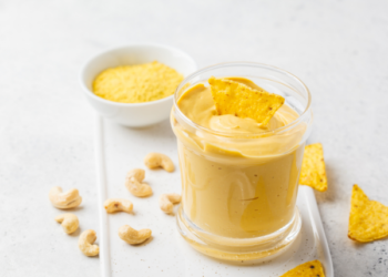 Yellow vegan cheese dip made from cashews with a tortilla chip dipped into