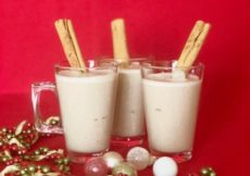 3 cups of coquito on a red background with Christmas ornaments around