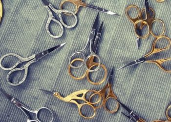 Collection of embroidery scissors on a grey corduroy background.