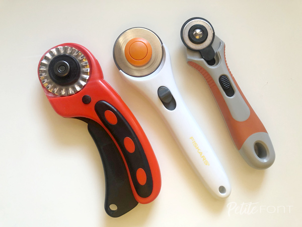 Selection of 3 different rotary cutters: an ergonomic handled red one with pinking blade, a straight white one with regular blade, and a small grey and orange one with a smaller blade