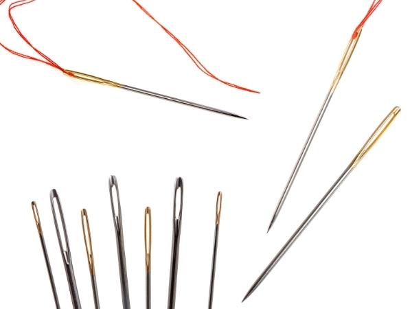 A variety of hand sewing needles, some threaded with red thread, on a white background