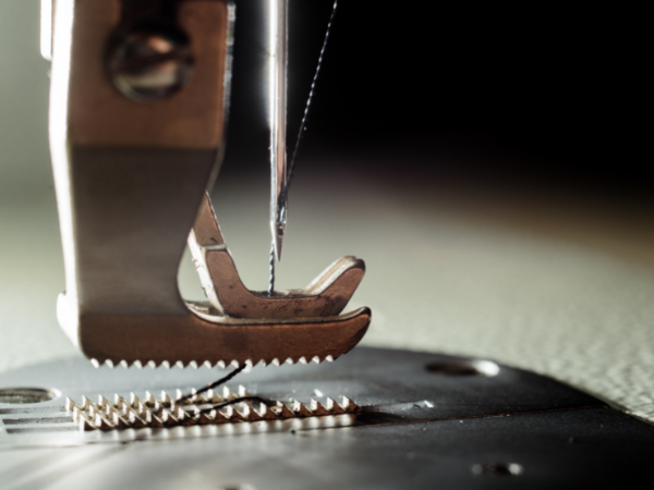 Close up view of a sewing machine needle lifted to the top position, with thread passing through the eye